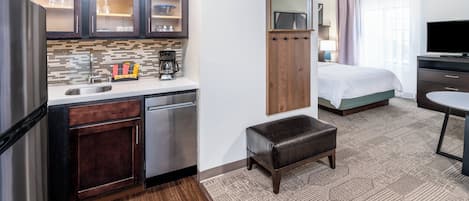 A compact hotel room with a kitchenette, a bed, a TV, and a small seating area.