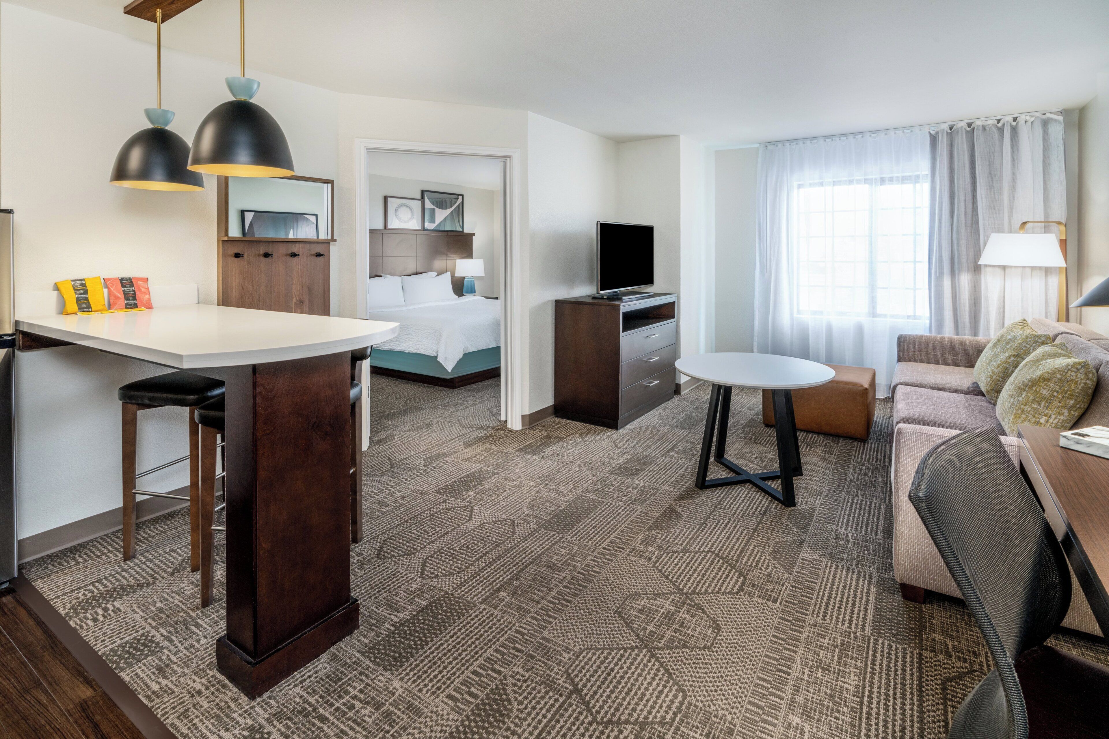 A hotel room with a bed, a desk, a sofa, a TV, and a dining area.