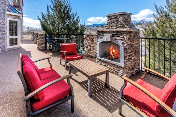 Un patio al aire libre con muros de piedra, una chimenea, sillas rojas y una mesa.