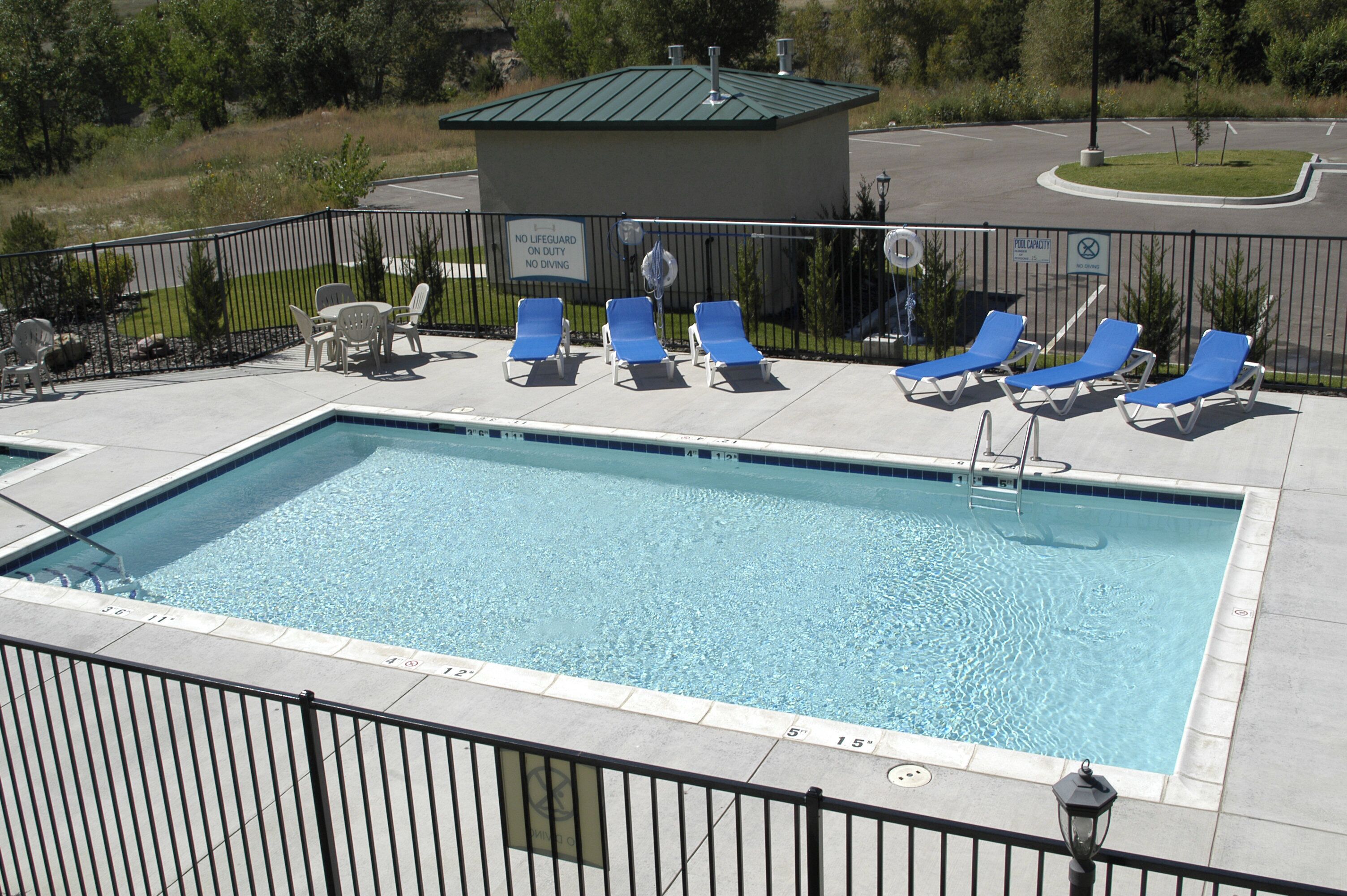 Une piscine rectangulaire à l’eau d’un bleu limpide, entourée d’une clôture en métal noir. Plusieurs chaises longues bleues sont alignées le long du bord de la piscine.