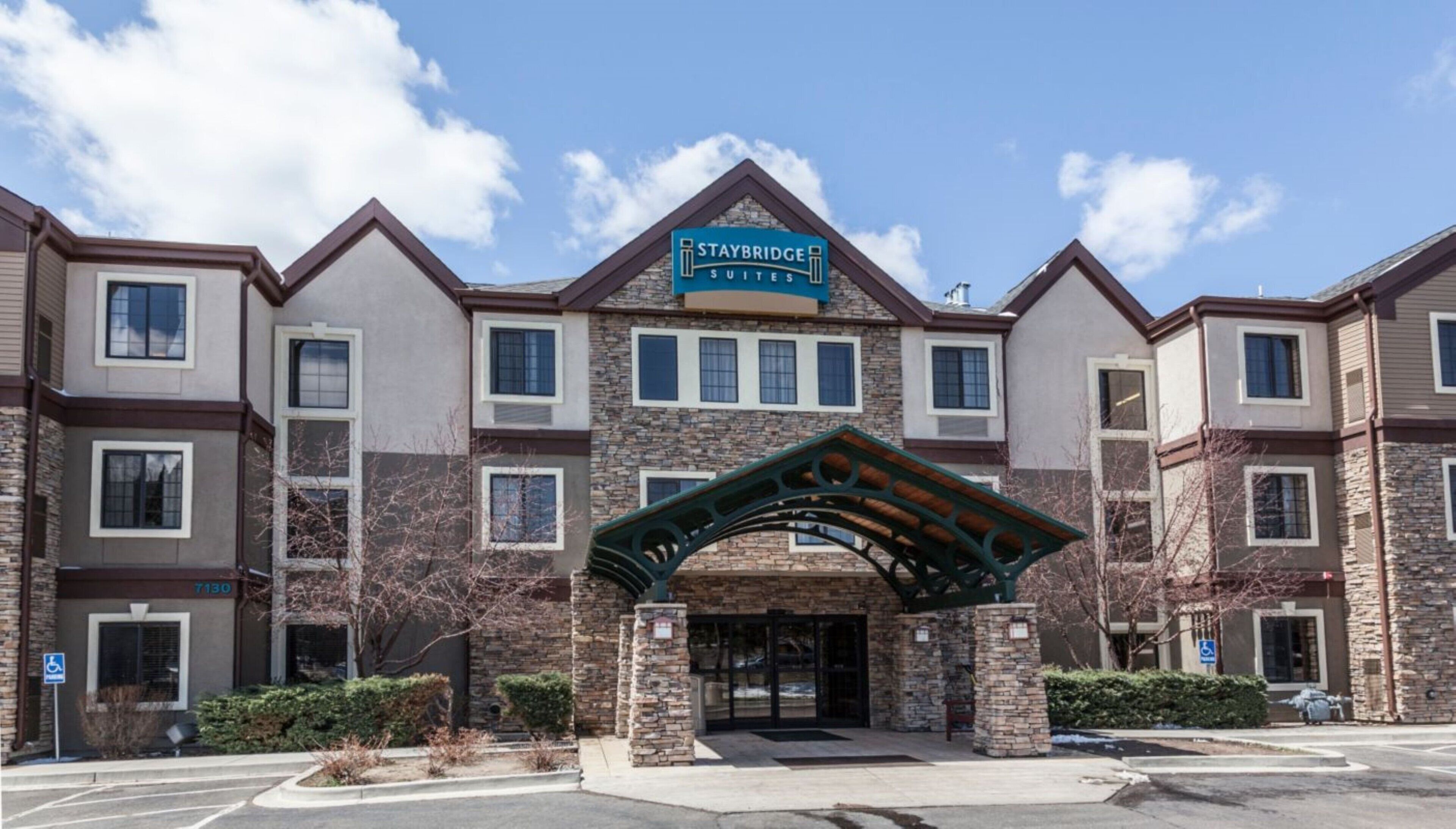 Un hôtel Staybridge Suites doté d’une façade en pierre, de nombreuses fenêtres et d’une entrée abritée.