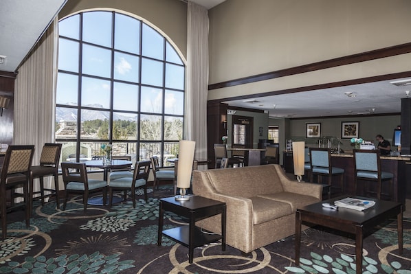A hotel lobby with a large window, a seating area with a sofa and chairs, a dining area with tables and chairs, and a reception desk. - Staybridge Suites Colorado Springs North by IHG (Colorado Springs)