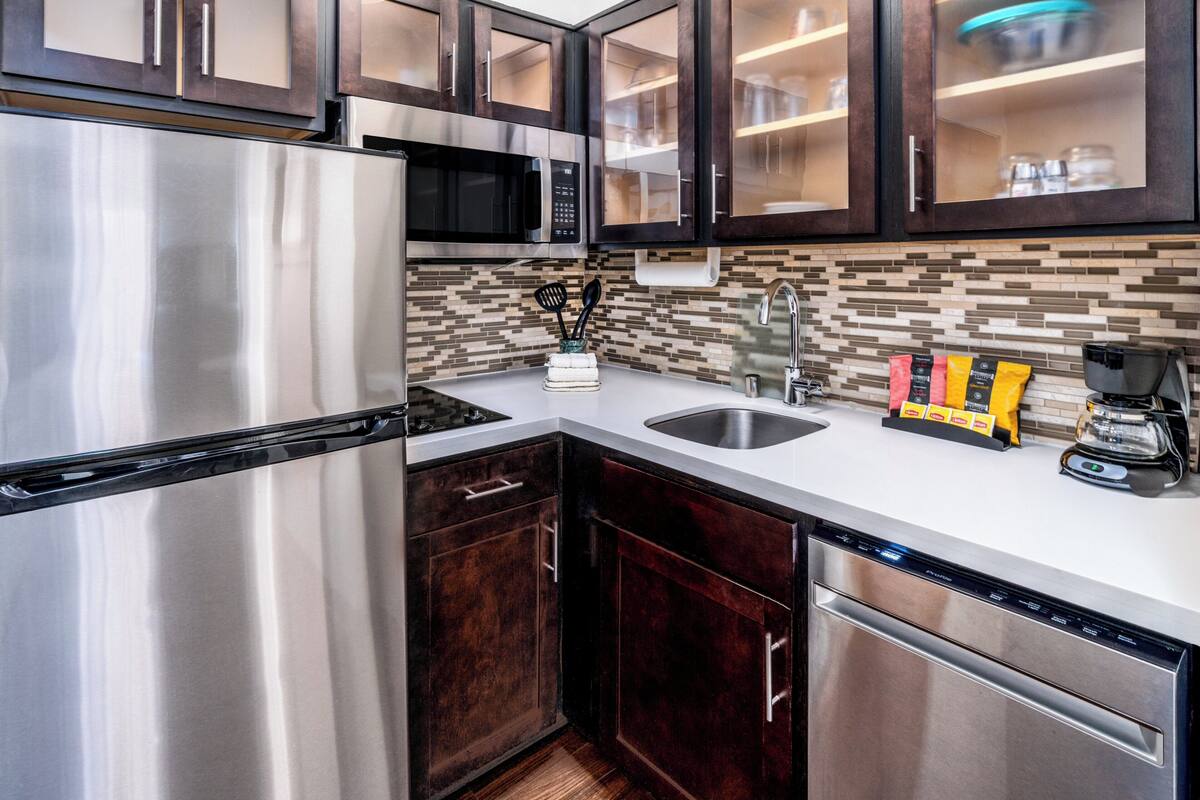 Una cocina moderna con electrodomésticos de acero inoxidable, armarios de madera oscura y un salpicadero de azulejos.