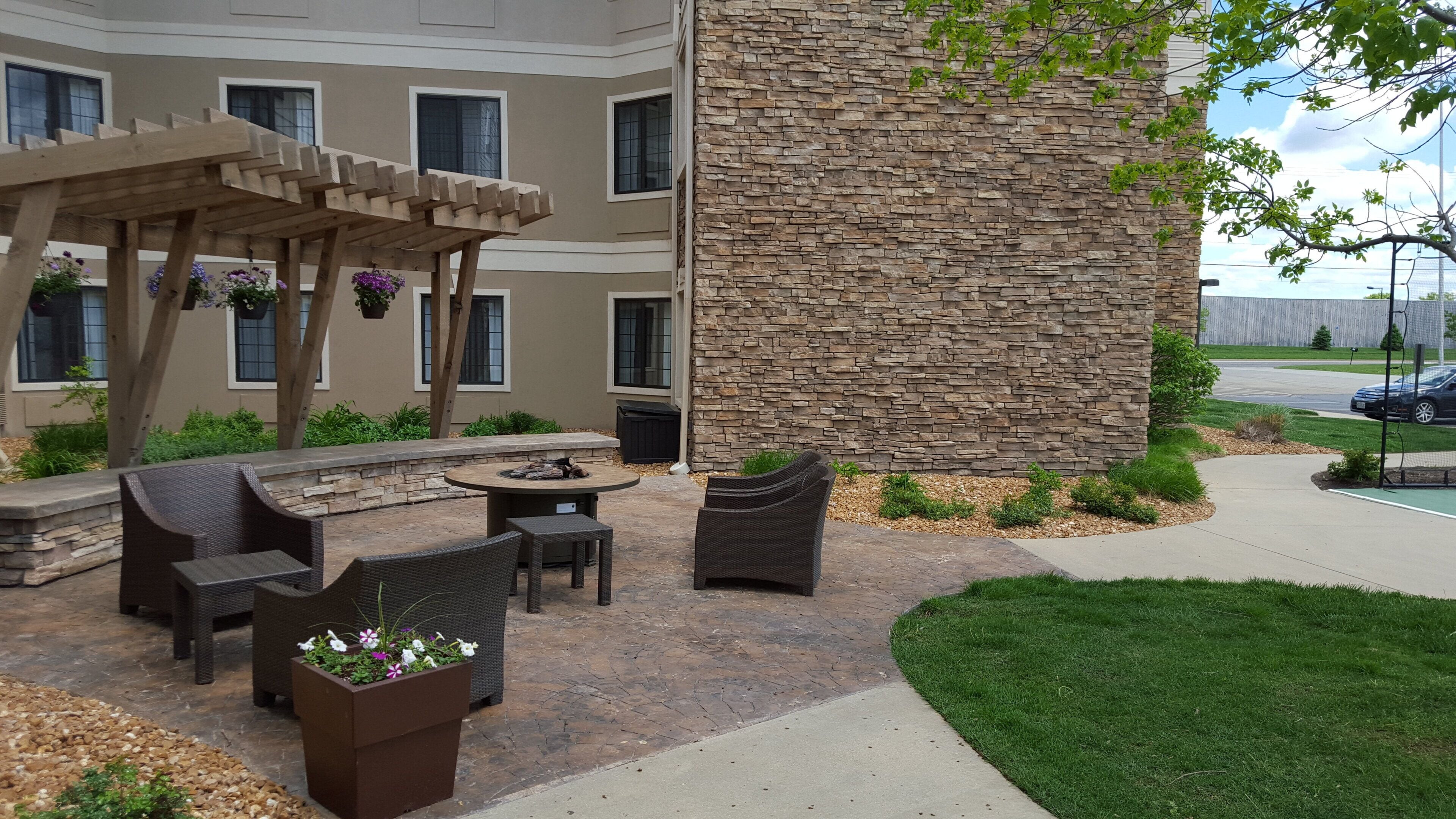 Un patio exterior con mobiliario de mimbre, una pared de piedra y una pérgola con macetas colgantes.