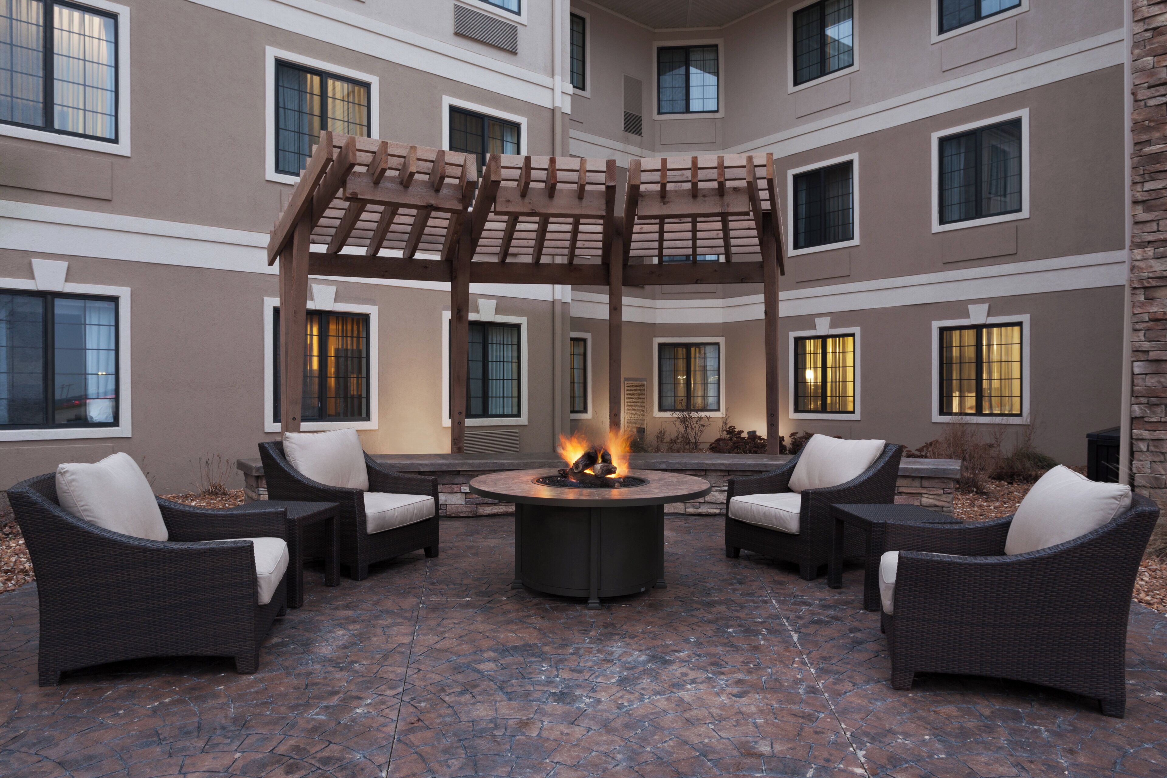 A courtyard with a fire pit, wicker furniture, and a pergola.