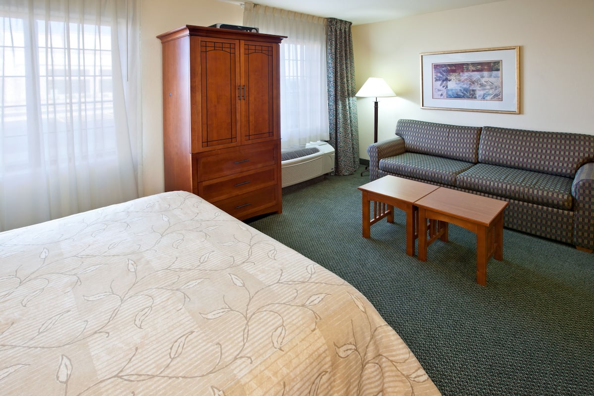 A hotel room with a large bed, a wooden wardrobe, a sofa, a small table, and a lamp.