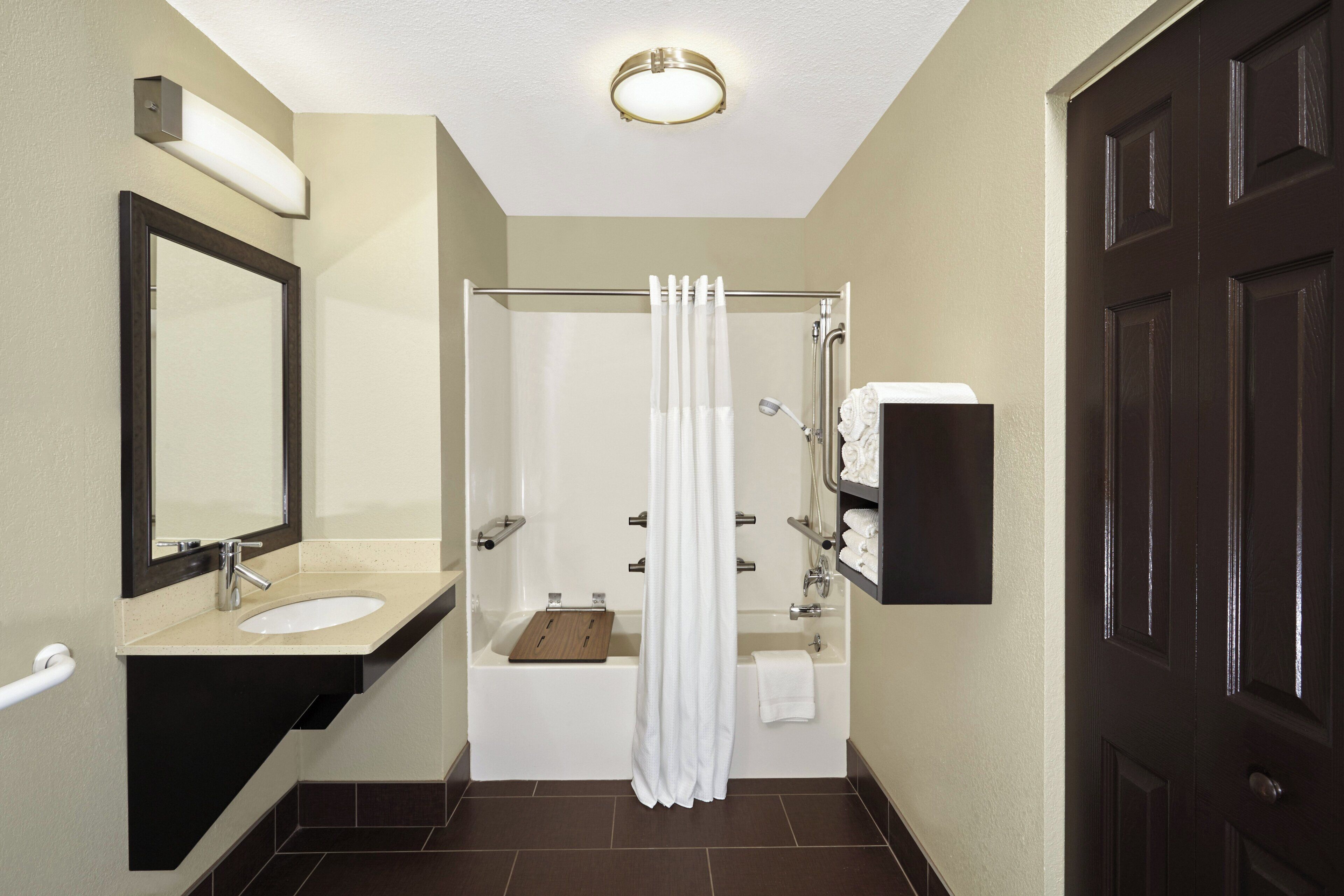 A bathroom with a sink, mirror, shower, and towel rack.