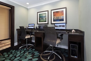Habitación de hotel con dos escritorios, cada uno con una computadora y una silla. Hay dos cuadros en la pared.
