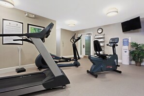 A fitness room with treadmills and elliptical machines, a clock, a water dispenser, and a TV mounted on the wall.