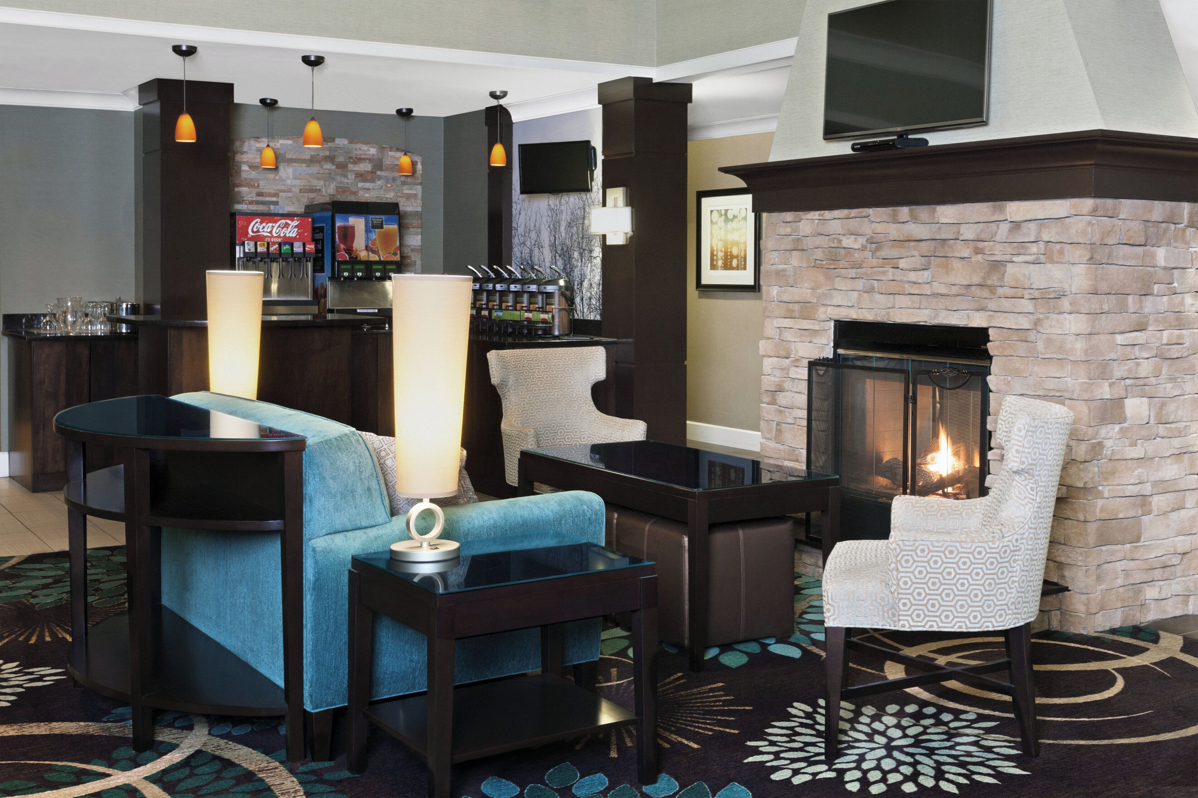 A lobby area with a seating arrangement, a fireplace, a bar with a Coca-Cola machine, and a television mounted on the wall.