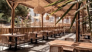 Een openluchtrestaurant met houten tafels en rieten stoelen, overdekt met een rieten dak.