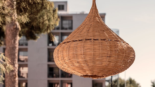 Een zwembadgedeelte met ligbedden en parasols, een hangende rotanlamp en een modern gebouw op de achtergrond.