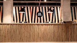 Een receptiegedeelte met een wand van bamboe panelen, een 'CC Cook's Club'-bord en hanglampen.
