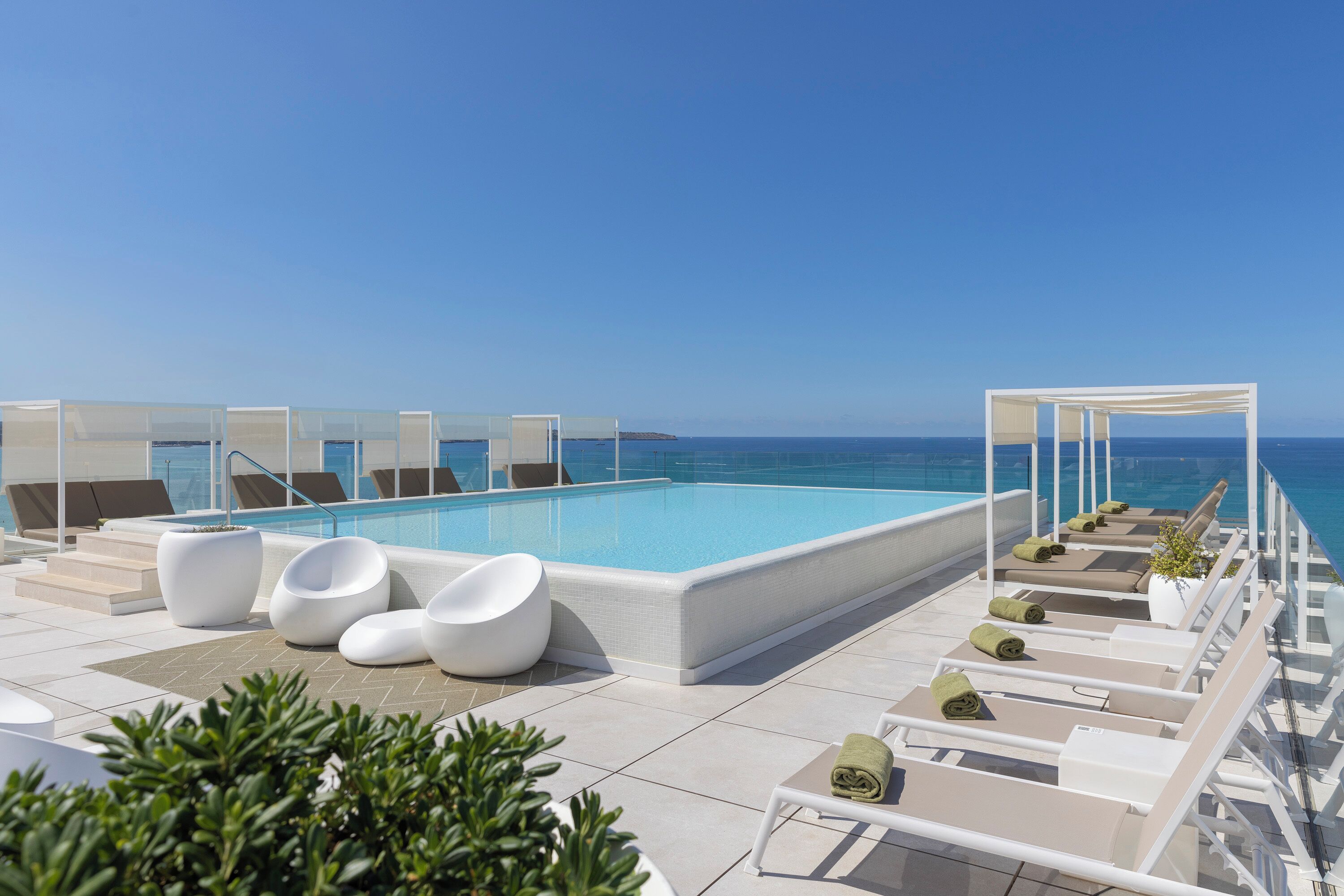 A rooftop pool area with lounge chairs and a clear view of the ocean.