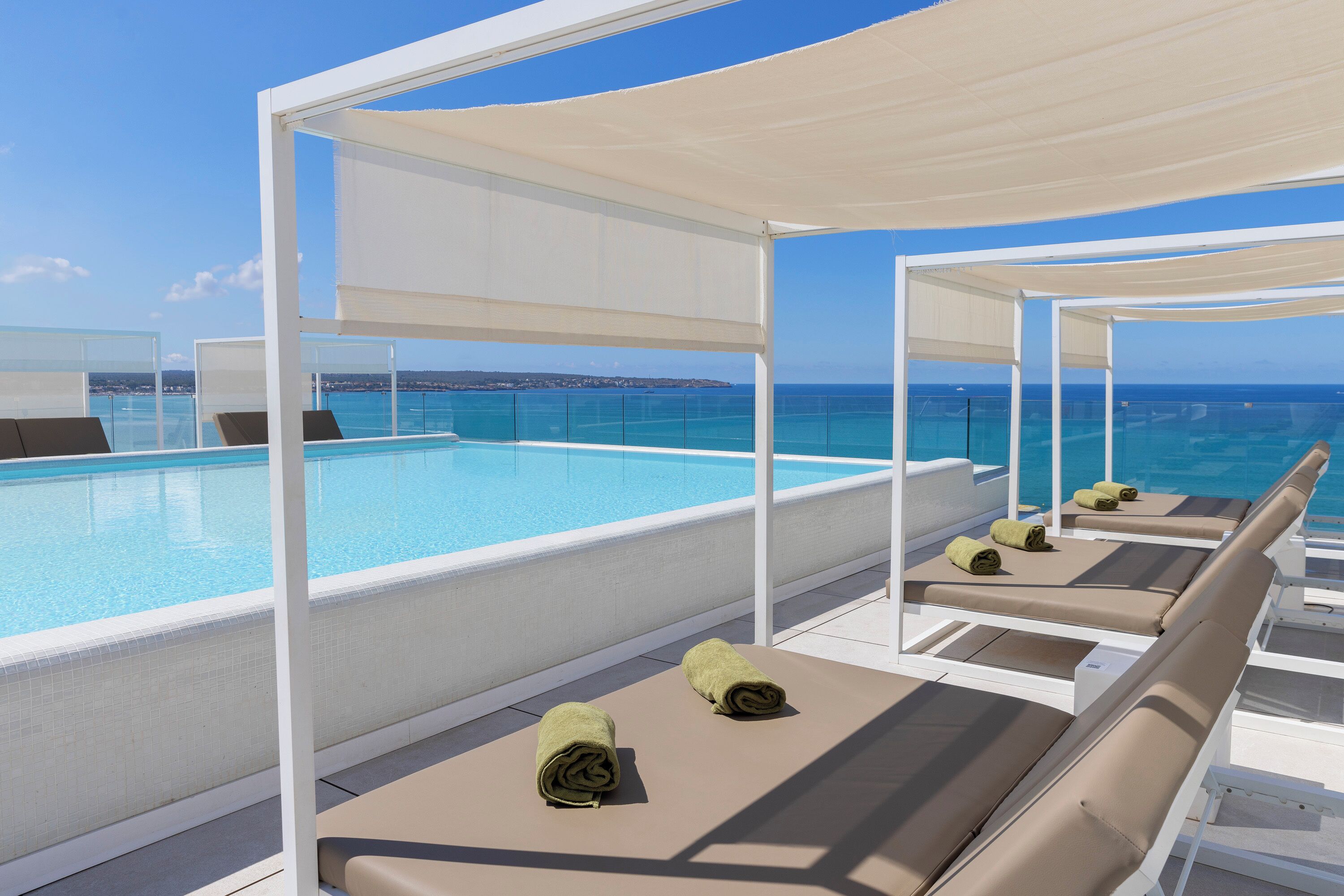 A rooftop pool area with sun loungers and a clear view of the ocean.