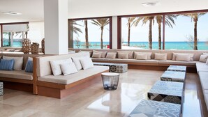 Una sala de estar moderna con un ventanal grande que da a una playa, que incluye un conjunto de sofás, una mesa de centro y mesitas de noche estampadas.