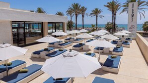 Zona de piscina de hotel con sillones de descanso y sombrillas, con vista al mar.