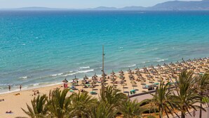 Una playa con filas de sombrillas y tumbonas, un mar azul cristalino y palmeras.