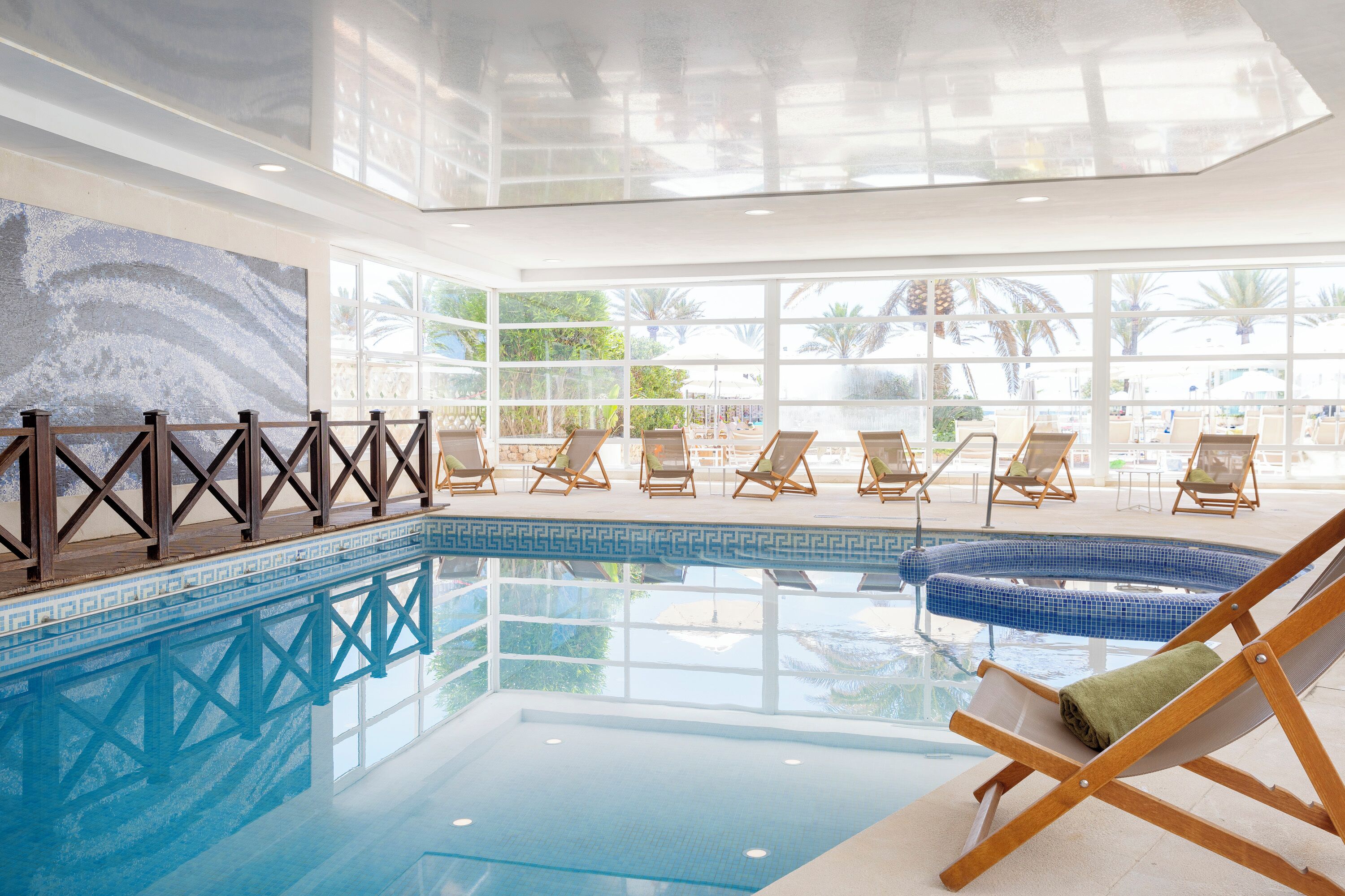 An indoor swimming pool with lounge chairs and a view of the outdoors.