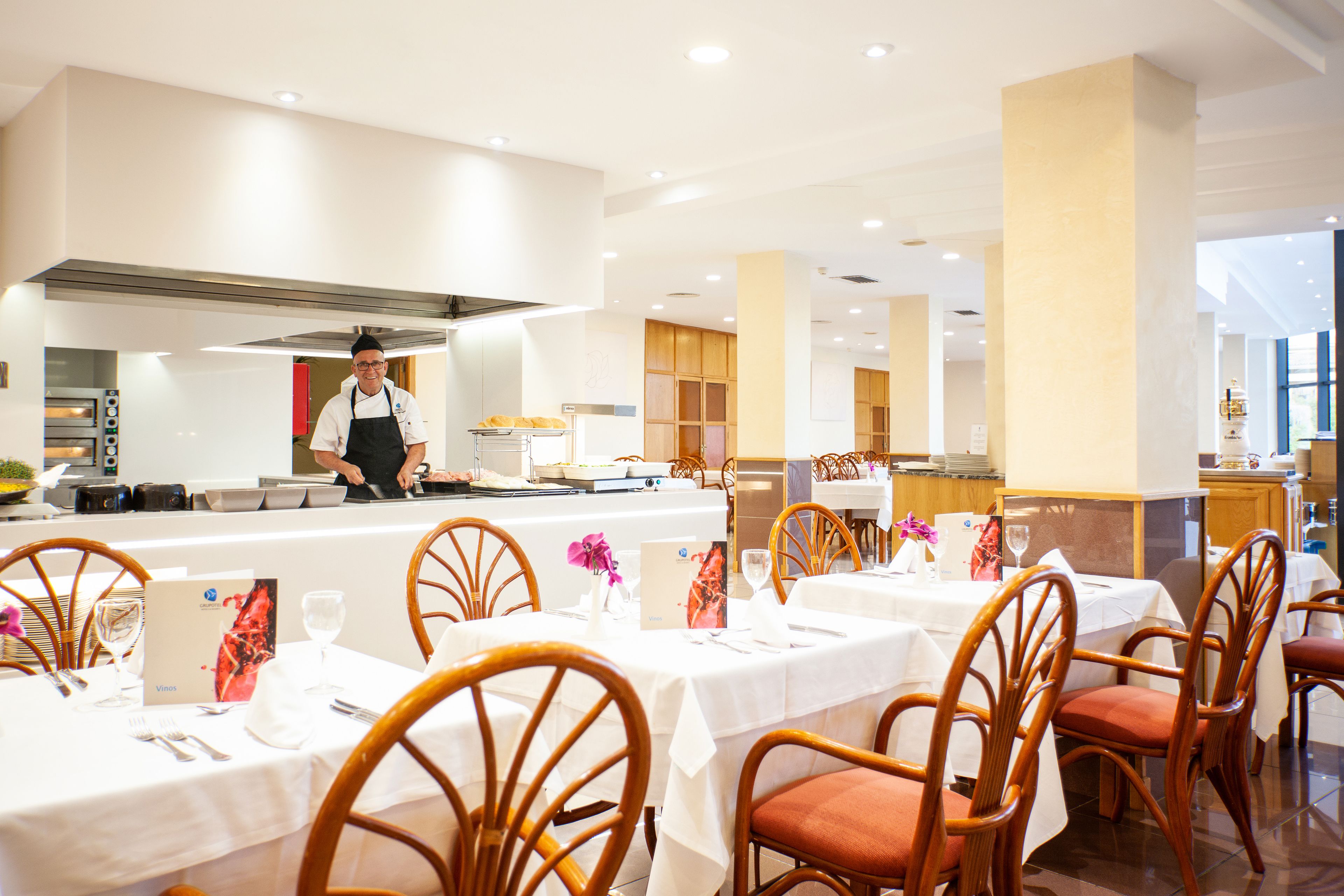 A restaurant with tables set for dining, a chef at the counter, and a kitchen in the background.