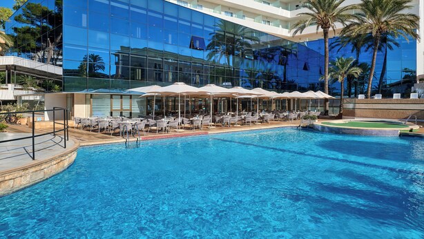 A hotel with a large reflective glass facade, a swimming pool with lounge chairs, and palm trees. - Grupotel Taurus Park (Palma de Mallorca)