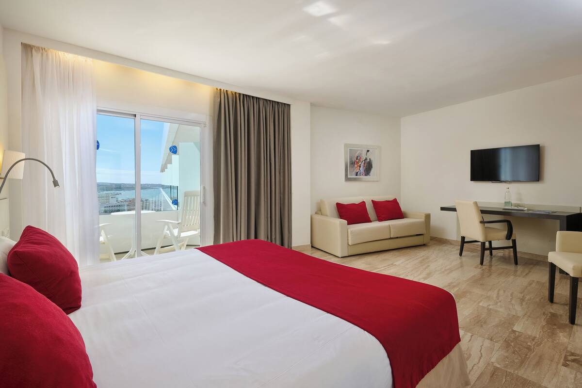Quarto de hotel com uma cama grande, uma escrivaninha, um sofá e uma televisão.