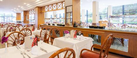 Restaurante com várias mesas, cadeiras de madeira e uma área de buffet.