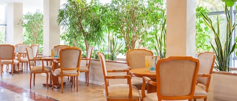 A spacious indoor area with wooden chairs and tables, surrounded by large potted plants.