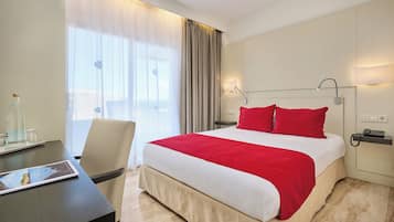 Hotelkamer met een groot bed, een bureau en een stoel. Er is een raam met gordijnen, een lamp en een telefoon op het nachtkastje.