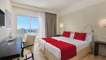 A hotel room with a large bed, a desk, and a chair. There is a window with a view of the city.