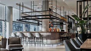 A modern bar area with a curved counter, multiple seating options, and a large potted plant. - Radisson Collection Hotel, Warsaw (Warsaw)