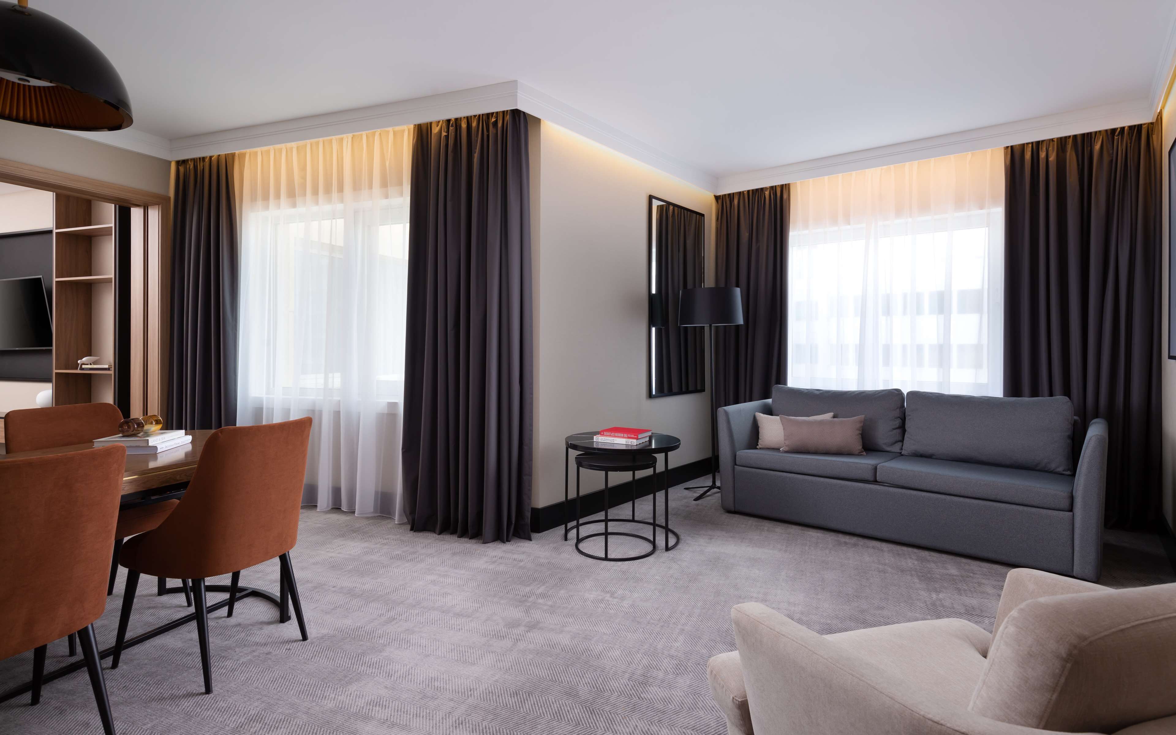 A modern hotel room with a dining area, a sofa, and a TV.