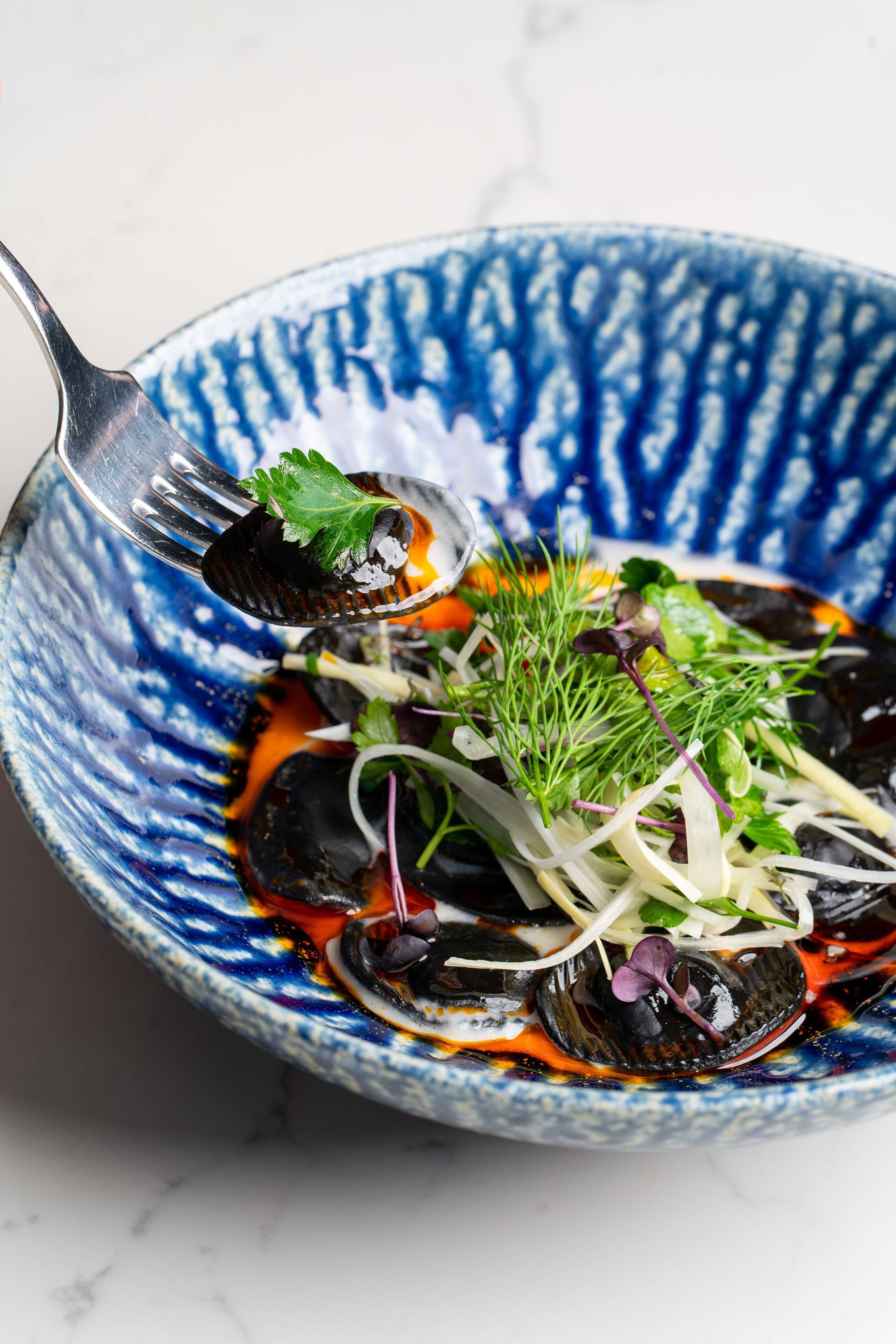 A bowl of food with a blue pattern, containing various vegetables and greens.