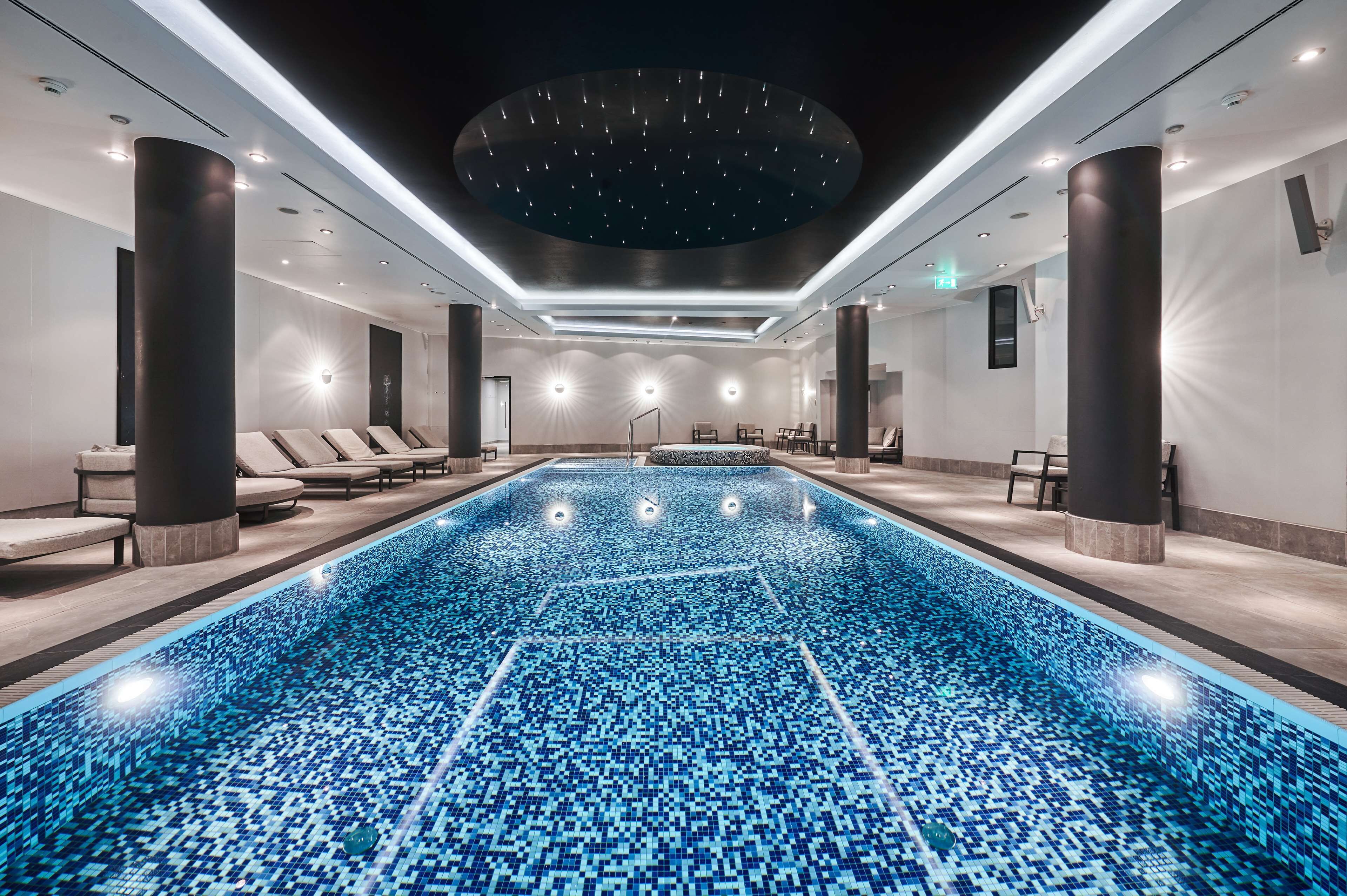 Una piscina interior moderna con techo estrellado, sillones de descanso y una lámpara con forma de sol.