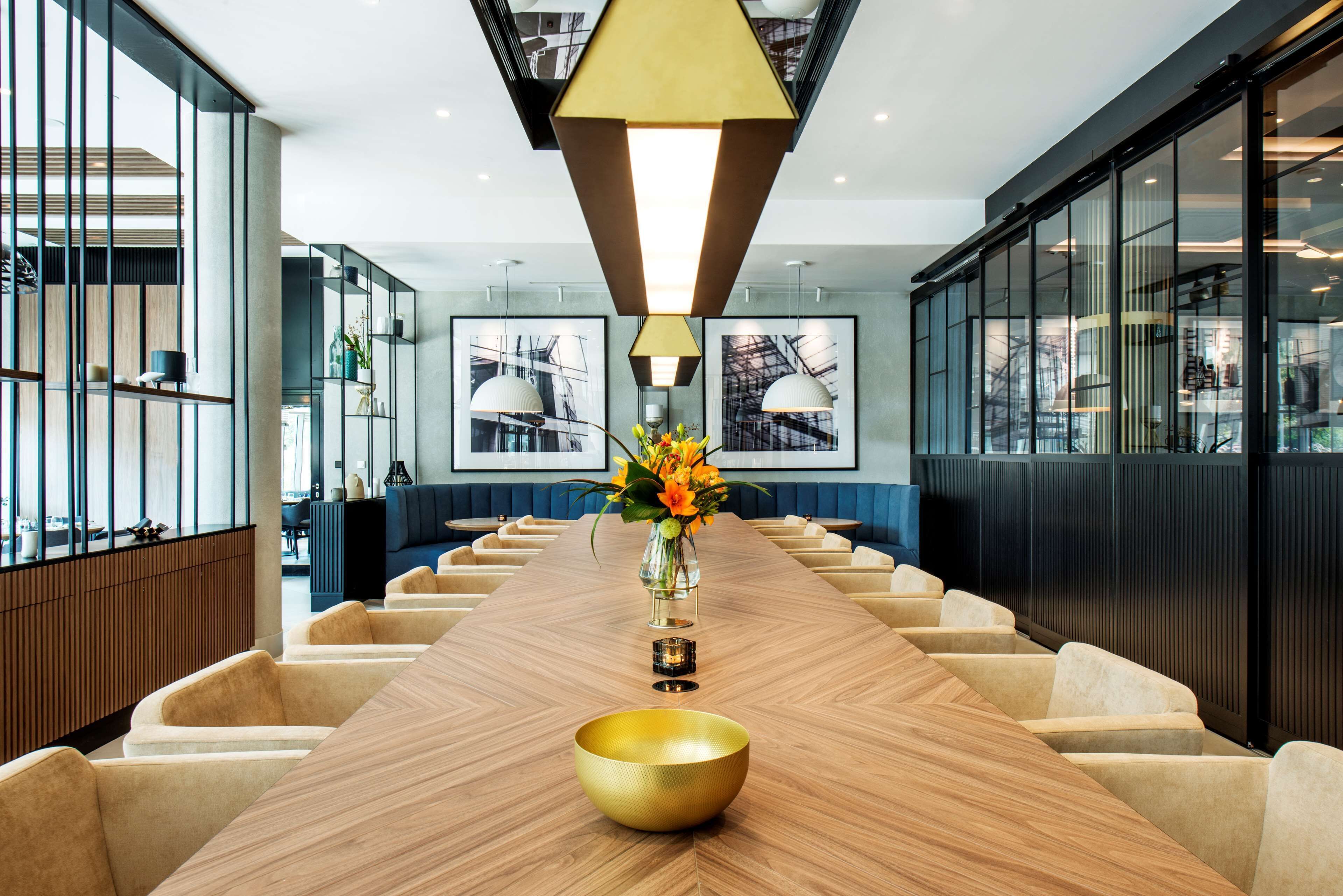 A modern conference room with a long wooden table, beige chairs, and a golden bowl centerpiece.