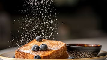 A slice of toast with blueberries on a plate, with a bowl of jam beside it.