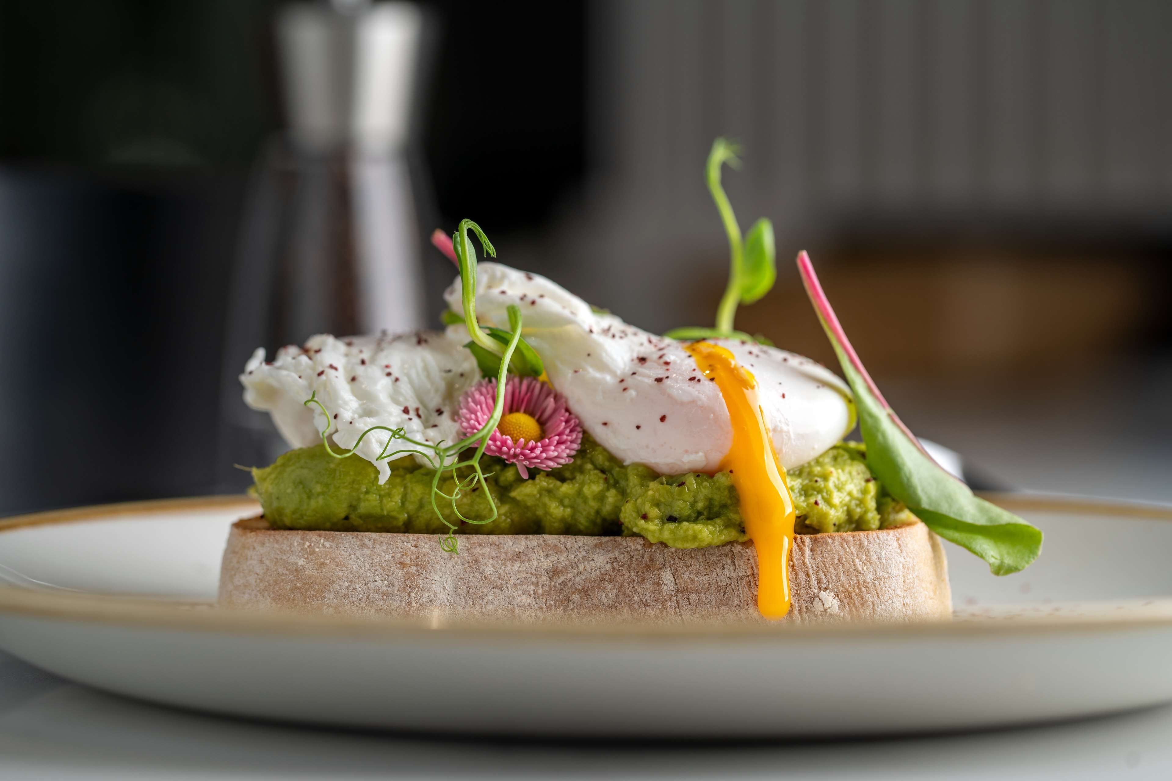 A dish with poached eggs, avocado, and greens on a slice of bread.
