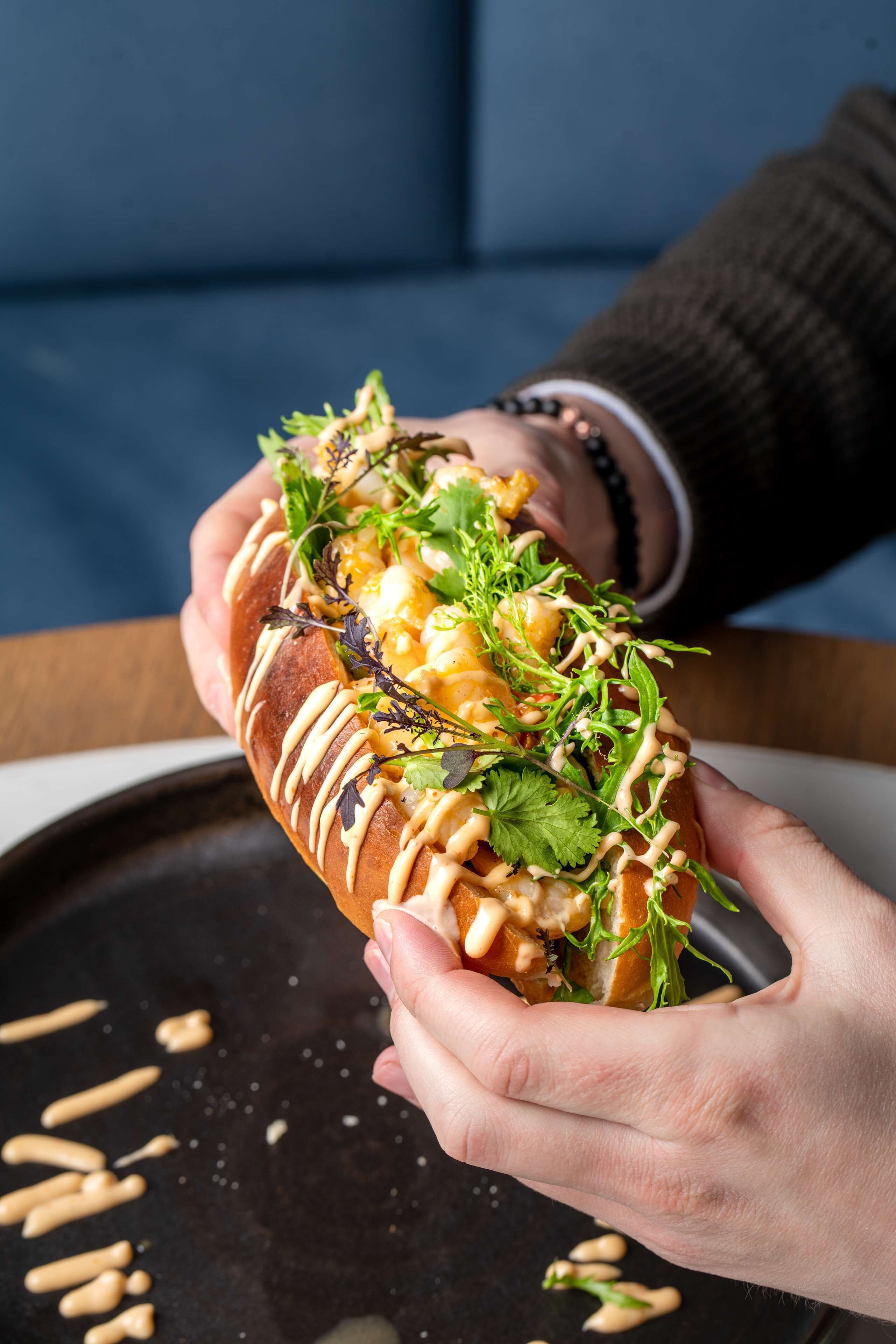 A person holding a sandwich with various toppings and sauces.