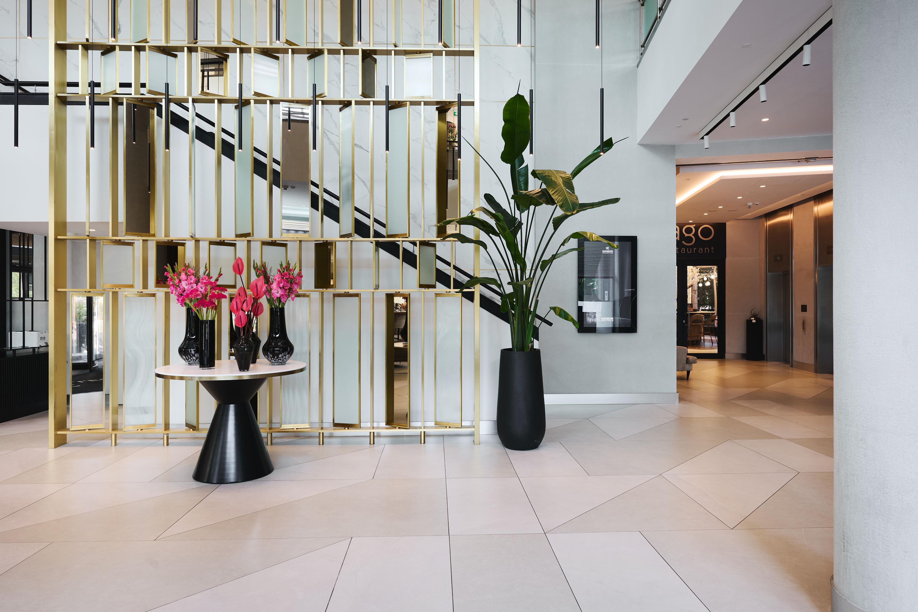 A modern lobby with a geometric decorative wall, a round table with vases, and a large potted plant.