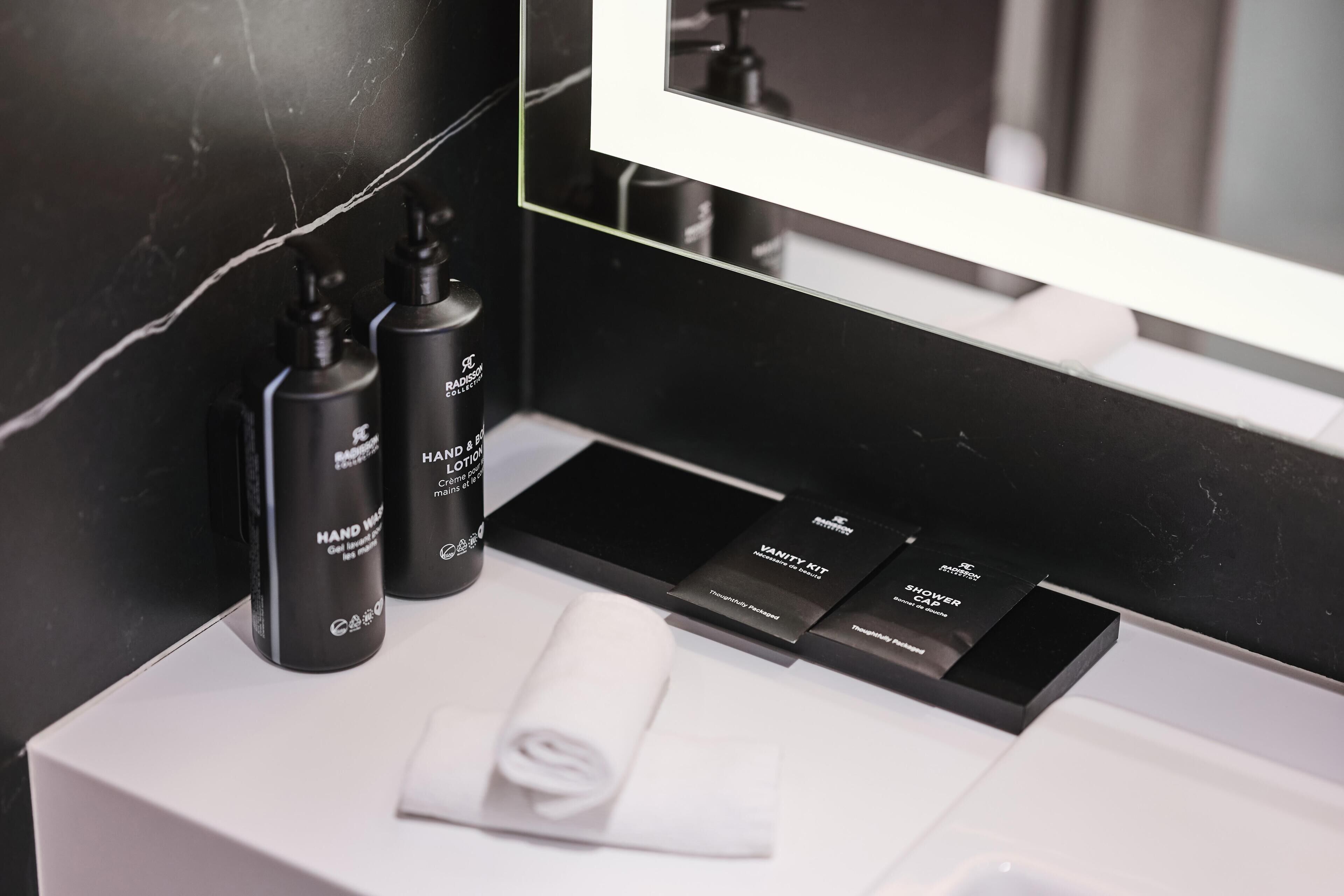A bathroom with a white sink, black marble walls, and a mirror reflecting a shower area.