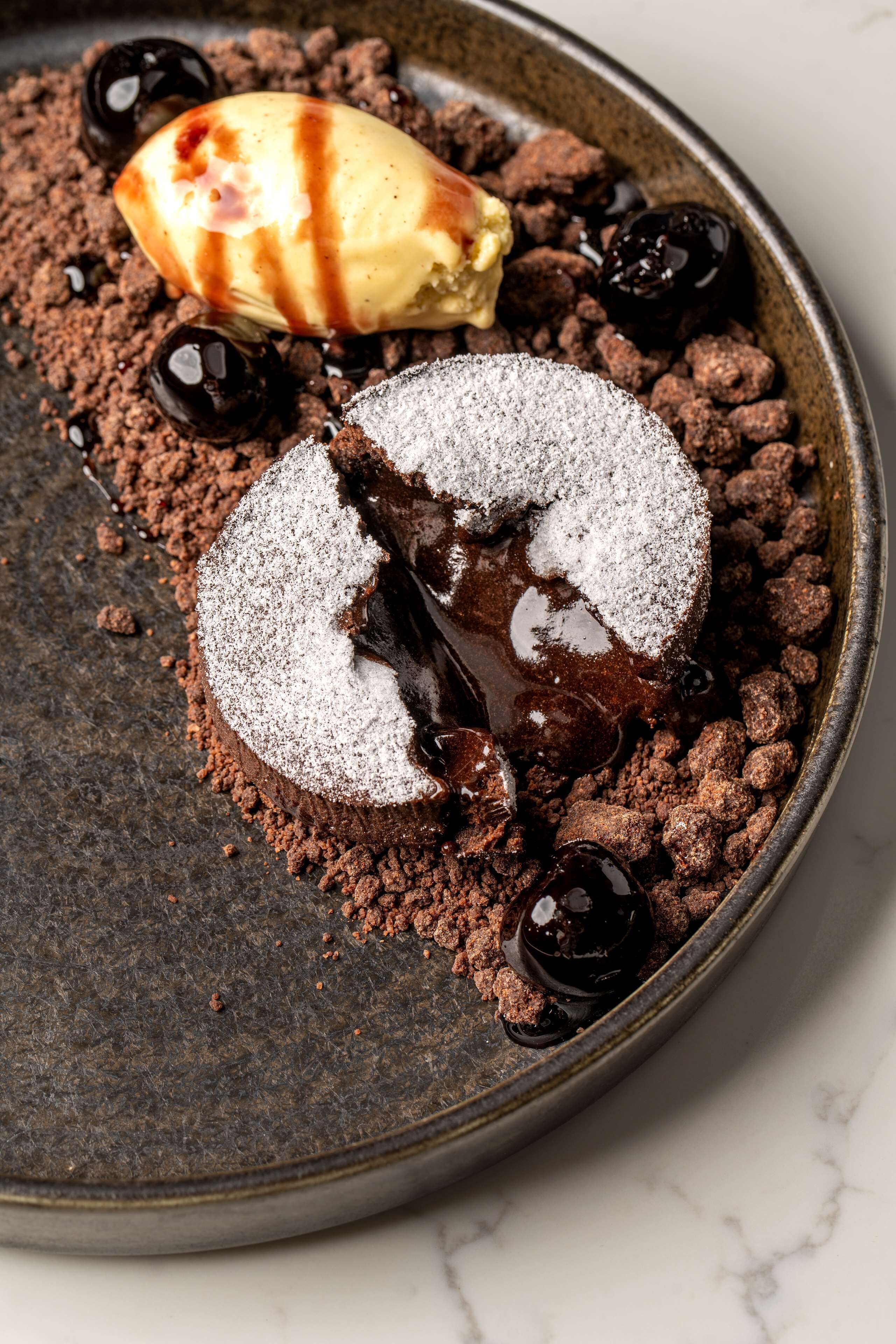 A dessert with chocolate crumble, a scoop of ice cream, and chocolate sauce.