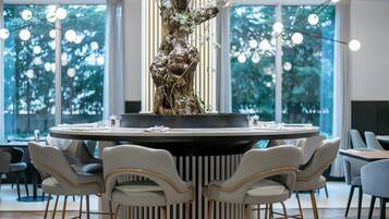 Una mesa redonda para comer con seis sillas, una escultura de árbol en el centro y vistas a árboles a través de amplias ventanas.