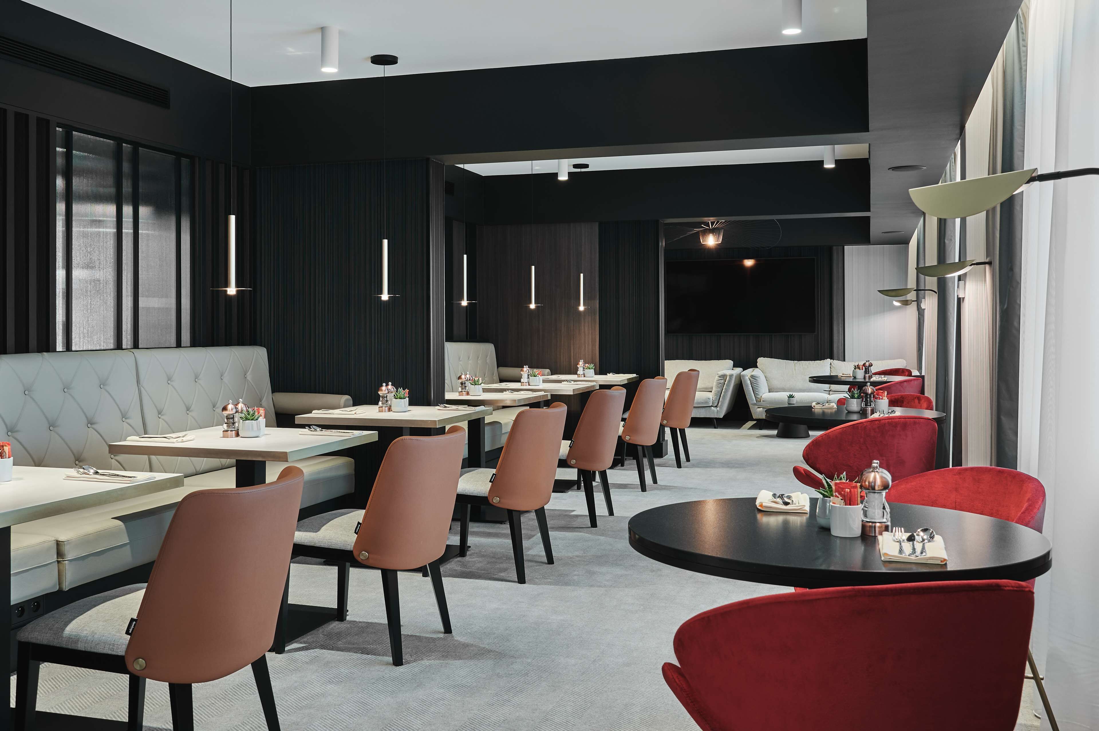 Un comedor moderno con mesas largas, asientos acolchados e iluminación colgante.