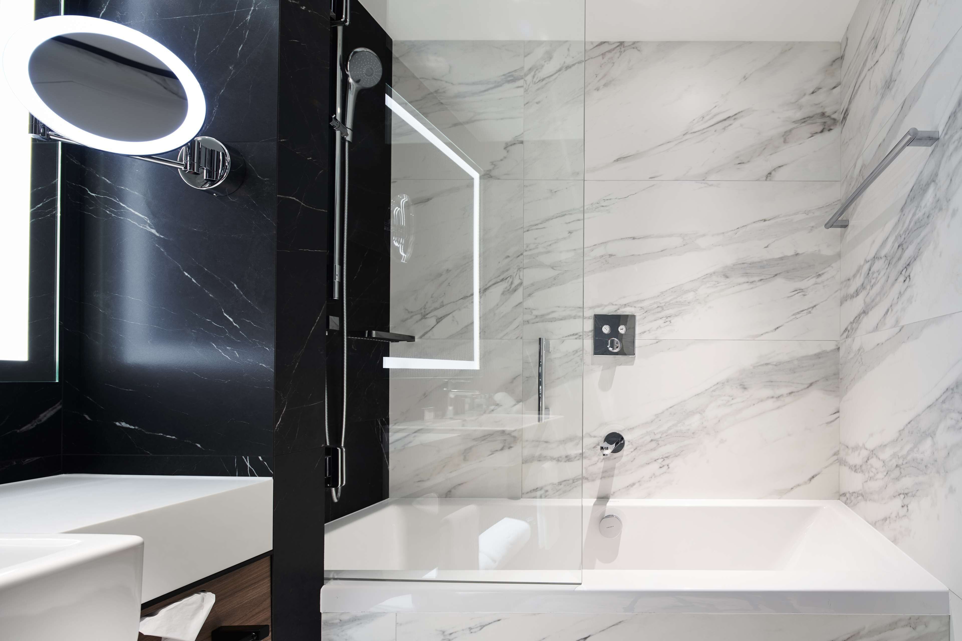 A modern bathroom with a glass-enclosed shower, a white bathtub, and a vanity with a mirror.