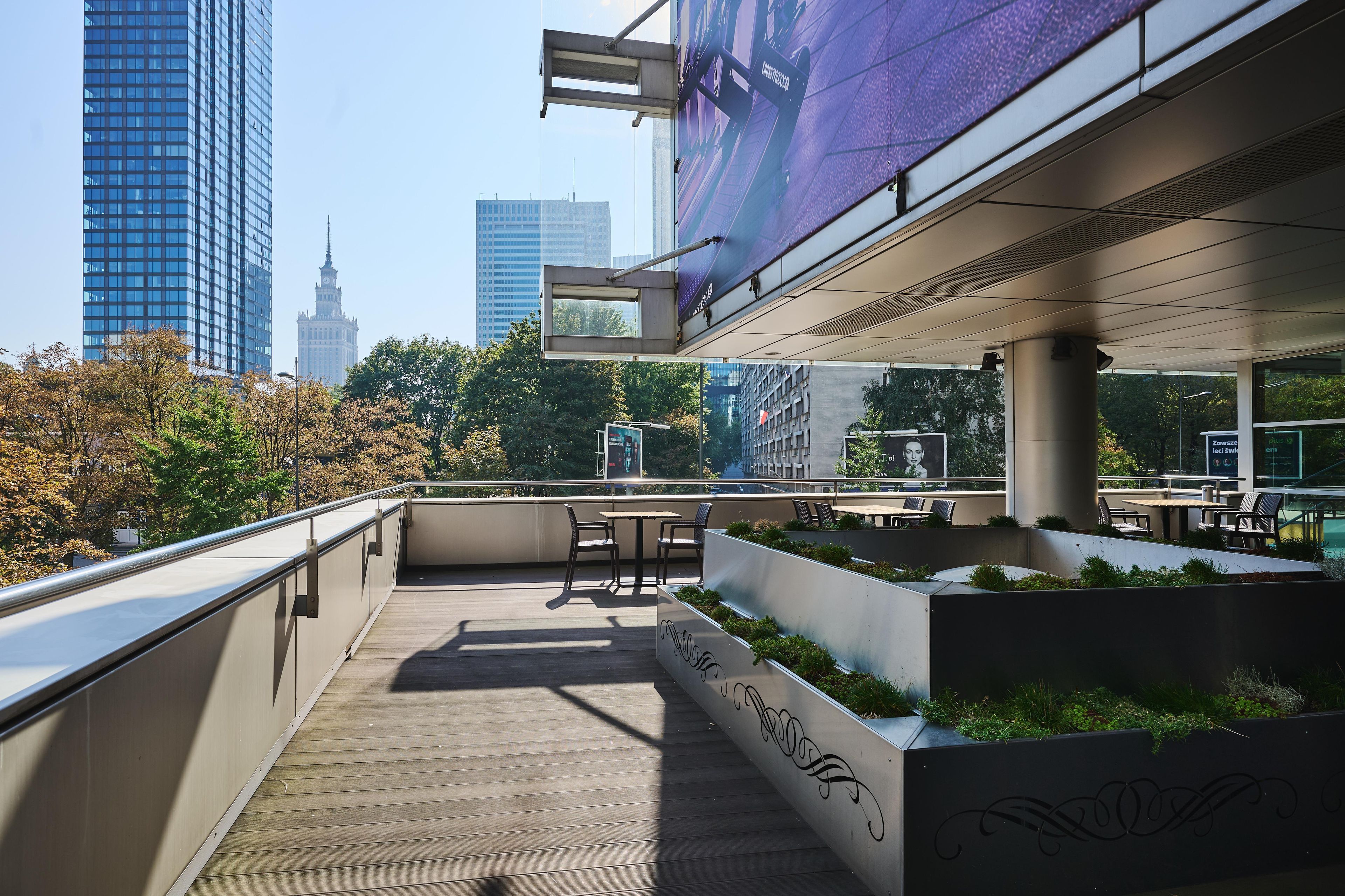Terraza al aire libre con mobiliario y macetas, con vistas a un paisaje urbano de edificios modernos.
