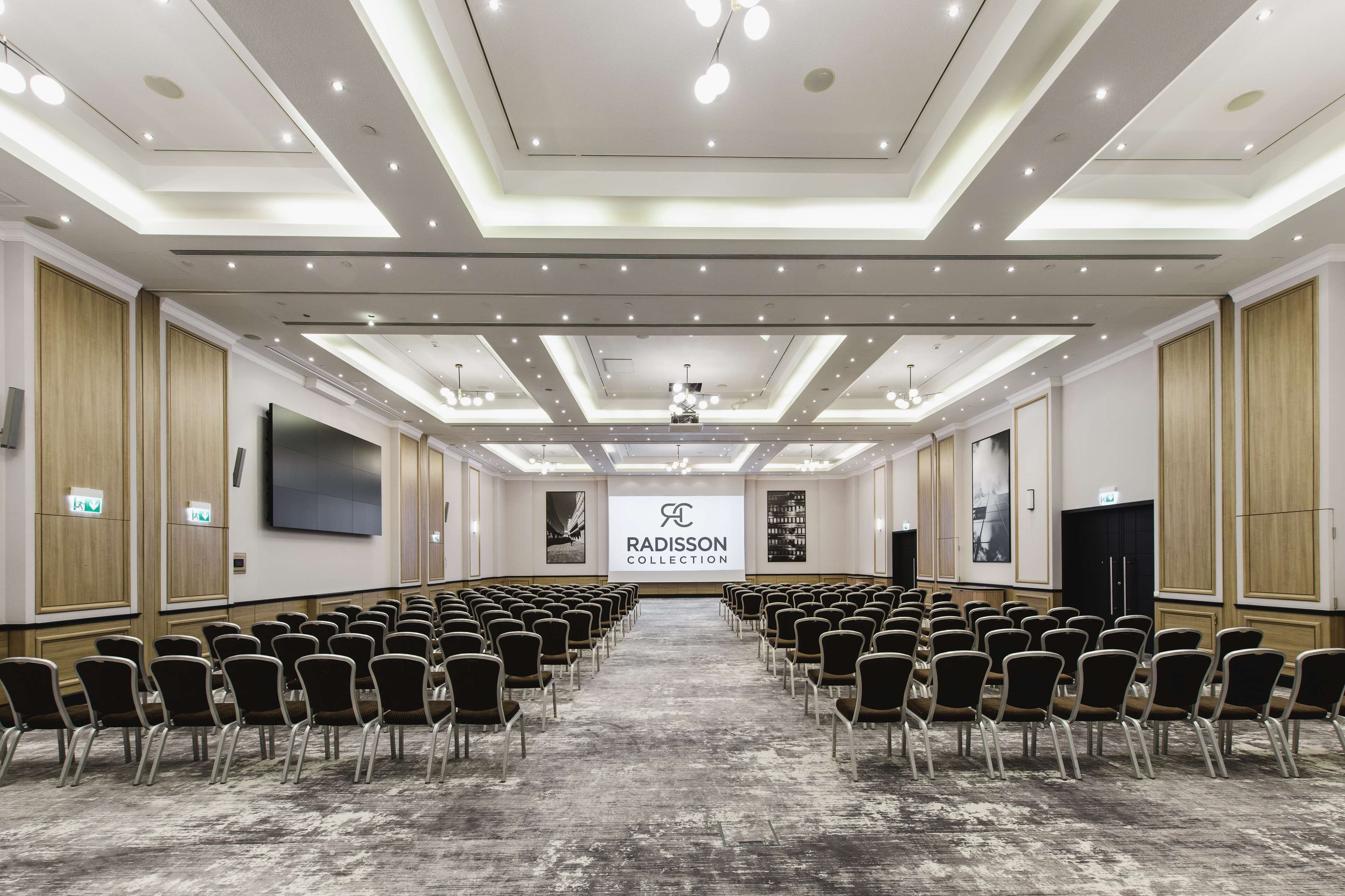 A conference room with rows of chairs, a stage with a presentation screen, and a Radisson Collection logo.