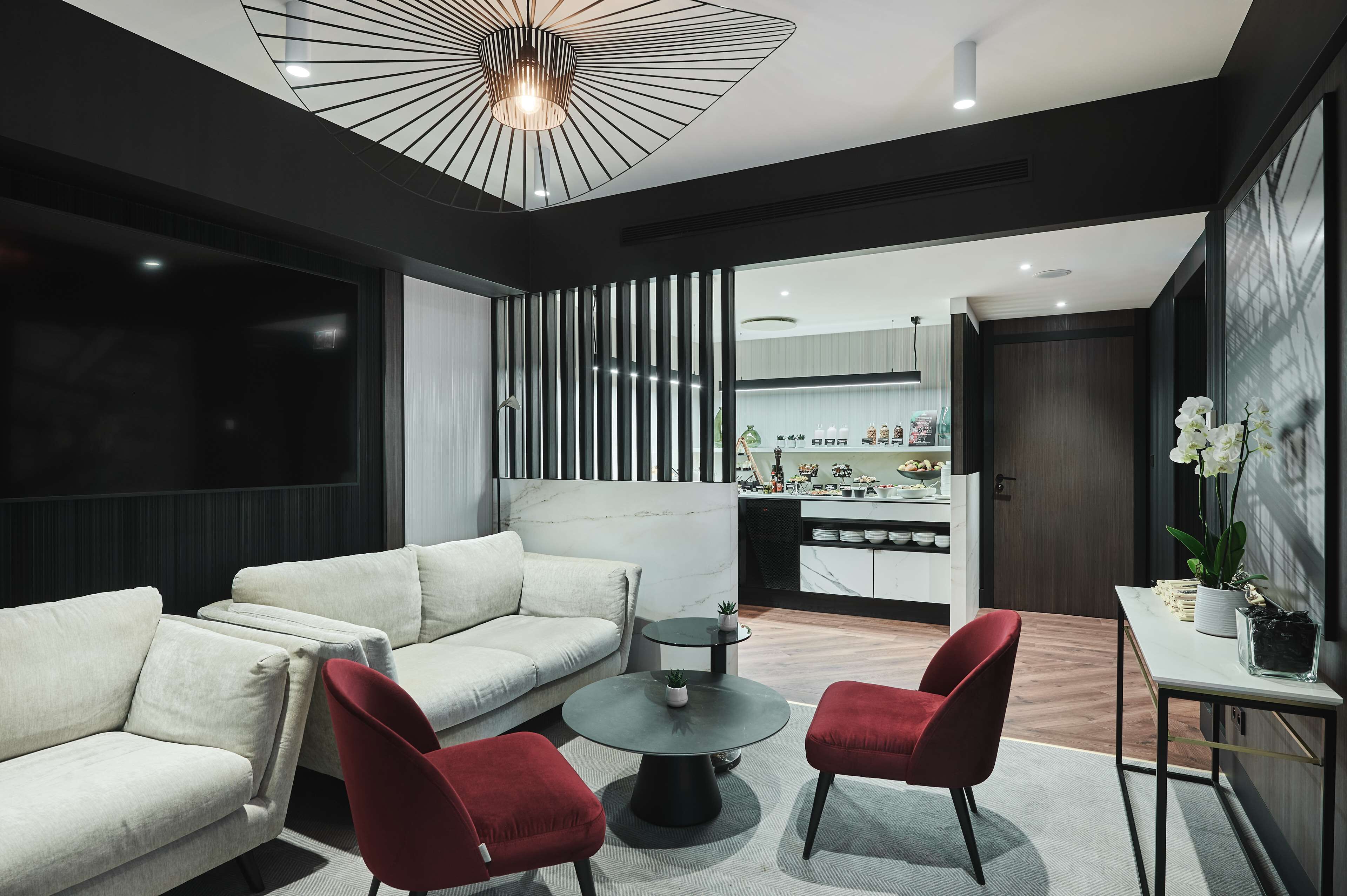 A modern living room with a sectional sofa, two red chairs, a round coffee table, and a dining table with a potted plant.