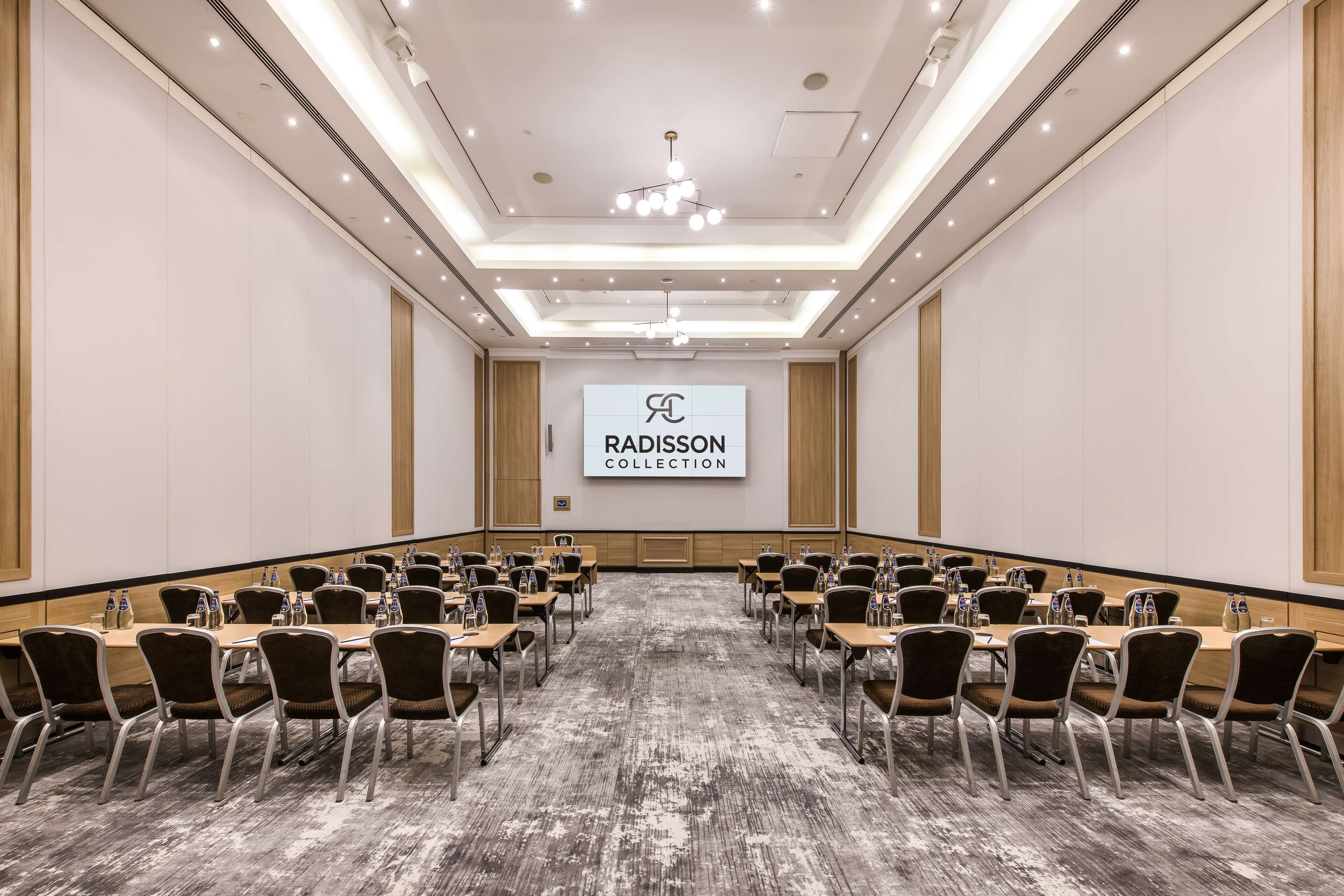 A conference room with a long table, chairs, and a screen displaying 'RADISSON COLLECTION'.