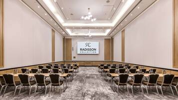 Konferenssihuone, jossa on pitkä pöytä, tuoleja ja näyttö, jossa näkyy teksti ’RADISSON COLLECTION’.