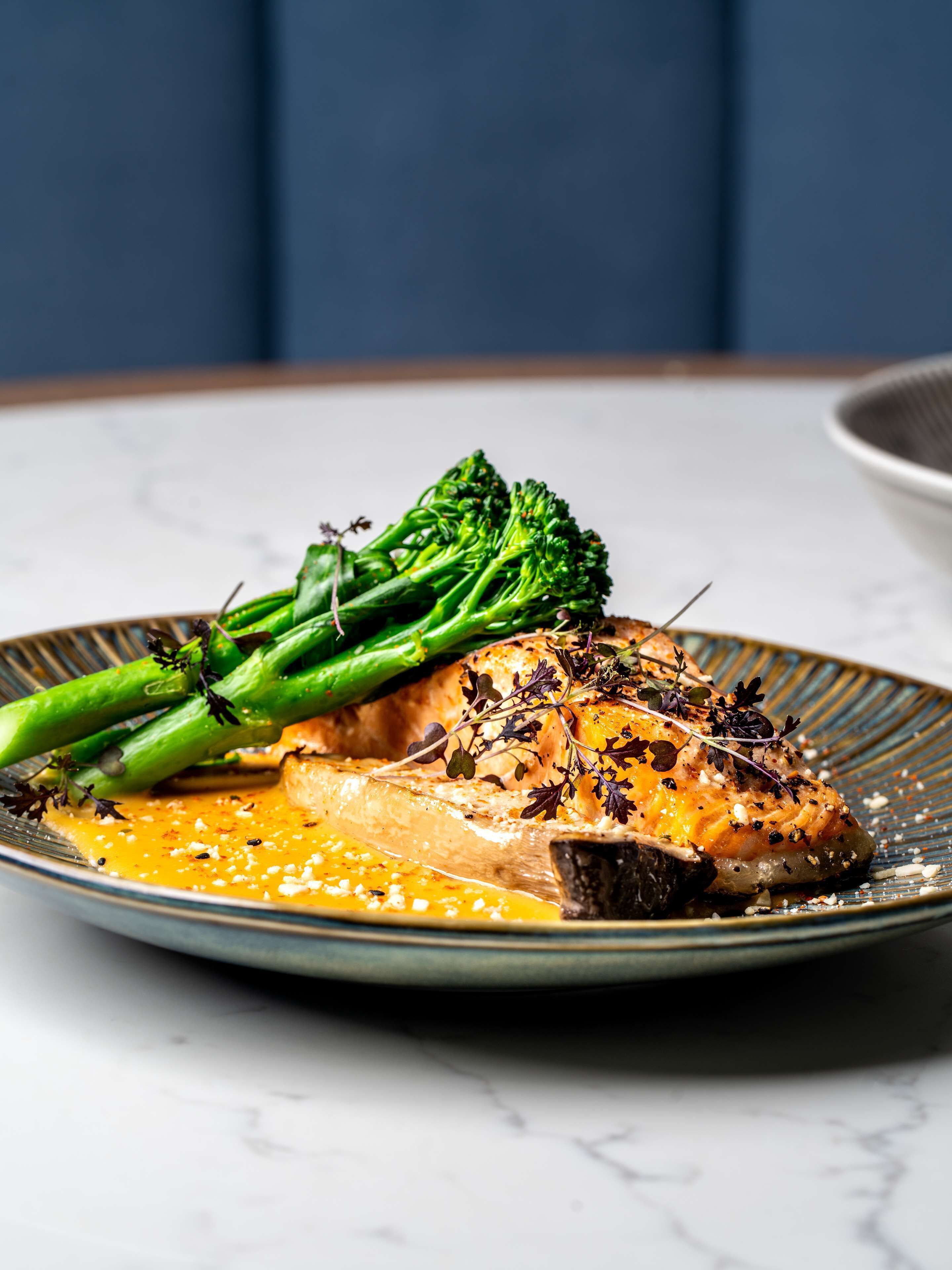 A plate with a piece of grilled chicken, a slice of lemon, and a side of broccoli.